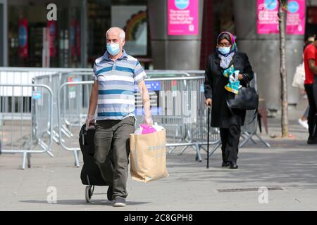 Gli acquirenti che indossano la maschera facciale come misura preventiva tengono le borse della spesa Primark a Londra. Foto Stock