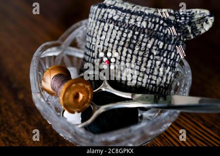 Attrezzi per gli abiti da indossare. Forbici, rocchetto di filo e perni in un vaso di cristallo. Foto Stock