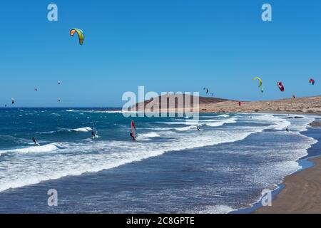 Montana Roja Beach Side con surfisti che si godono una giornata ventosa praticando sport acquatici come kite surf o kite boarding a El Medano, Tenerife, Spagna Foto Stock
