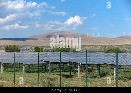 Impianto di generazione di energia elettrica, con diversi pannelli solari e turbine eoliche sullo sfondo, Foto Stock