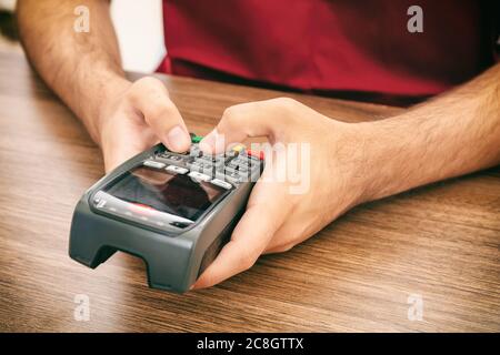 Uomo che tiene una macchina di scorrimento per il pagamento e che scrive, vista closeup. Lettore di carte di credito, concetto di pagamento terminale POS. Foto Stock