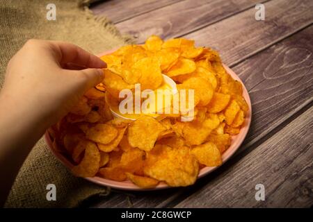 La ragazza prende un chip da un piatto rotondo con patatine e una pentola con salsa di formaggio al centro del piatto. Primo piano Foto Stock