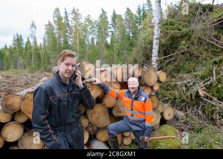 Uomo maturo che controlla legno tritato con felice giovane uomo usando il telefono fuori della foresta Foto Stock