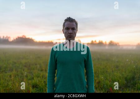 Giovane bell'uomo contro campo d'erba con nebbia nella pausa dell'alba Foto Stock