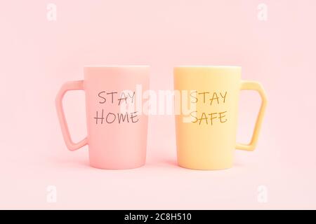 RIMANI A CASA e RESTA AL SICURO scritto su due tazze di caffè su sfondo rosa. Concetto sanitario, medico e di quarantena. Spazio di copia per il testo Foto Stock