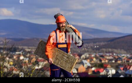 uomo che controlla tetto danneggiato. Costruttore qualificato installazione tegole. Lavori di costruzione con feltro per tetti. Tetto industriale. Ditta appaltatrice che posa tetto con casco protettivo. Giornata di sole. Foto Stock