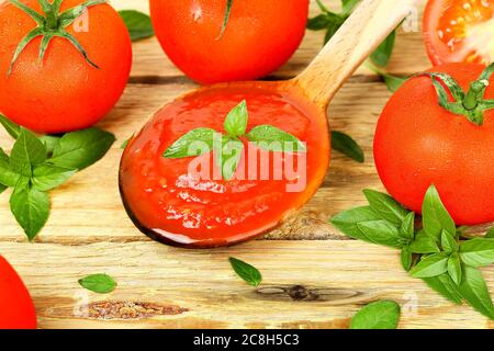 pomodori e mestolo di legno con salsa di pomodoro su legno Foto Stock