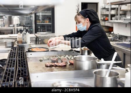 Chef in cucina uniforme in una cucina commerciale. Cuoca femmina che indossa grembiule in piedi da banco cucina che prepara il cibo. Foto di alta qualità.