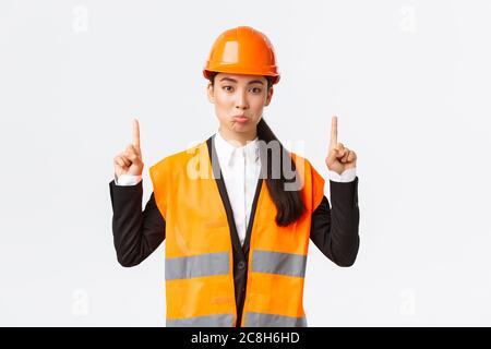 Costruzione, costruzione e concetto industriale. Dispiaciuto triste architetto femminile asiatica lamentando, indossando casco di sicurezza e abbigliamento riflettente Foto Stock