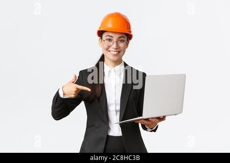 Sorridente felice ingegnere capo asiatico donna mostrando grafico con profitto impresa, facendo la presentazione durante gli investitori riunione, indossare casco di sicurezza Foto Stock