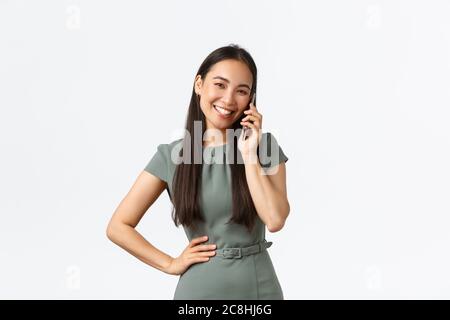 Proprietari di piccole imprese, donne imprenditori concetto. Sorridente donna d'affari riuscita in vestito che parla al telefono, tenendo smartphone e guardando Foto Stock