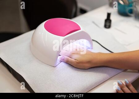 Primo piano bella donna mani e lampada per unghie sul tavolo. Salone gel unghie. Lampada UV. Processo di essiccazione del gel sulle unghie. Bellezza e cura di sé. Tecnologia moderna Foto Stock