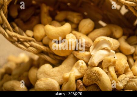 Noci di anacardi in un cesto di vimini e noci di anacardi sparse su tela di tela con una superficie di tessitura ruvida. Primo piano Foto Stock