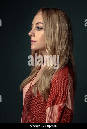 Ritratto di una donna trentenne penosa su sfondo scuro. Scatto in studio. Foto Stock