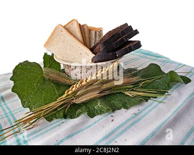 Pane affettato in un vaso, orecchio di grano e spikelets di cereali su una foglia di burdock. Isolato su sfondo bianco Foto Stock