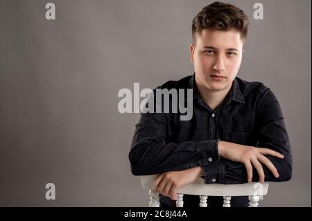 Primo piano ritratto di un uomo elegante e di grande stile vestito con una camicia nera casual che pacca sulla sedia isolata su sfondo grigio con spazio per la copia Foto Stock