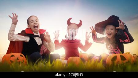 Ragazze felici su Halloween. Bambini divertenti in costumi di carnevale all'aperto. Bambini allegri e zucche sullo sfondo del tramonto. Foto Stock