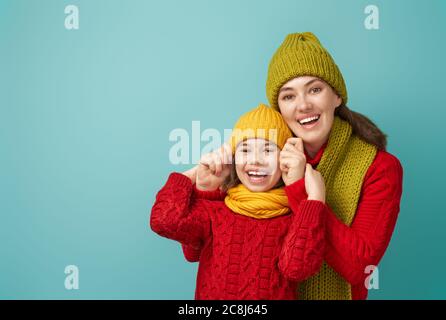 Ritratto invernale di famiglia felice e amorevole che indossa cappelli, snodi e pullover in maglia. Madre e bambina che si divertono, giocando e ridendo sul dorso del tepal Foto Stock