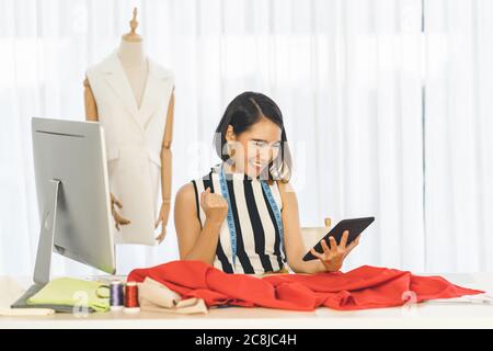 Giovane donna asiatica di designer che lavora e utilizza la tecnologia tablet sul posto di lavoro su vestiti manichini, avvio di piccole imprese, impresa entrep proprietario Foto Stock