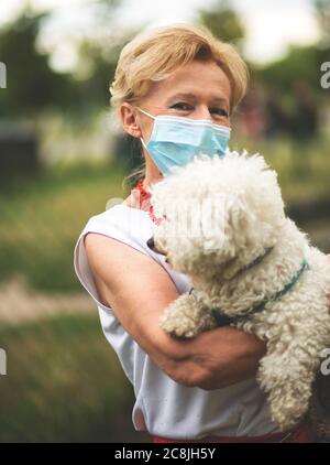 Ritratto di una bella donna bionda che indossa una maschera. Persone cani da passeggio, durante la pandemia di Covid-19, all'aperto. Foto Stock