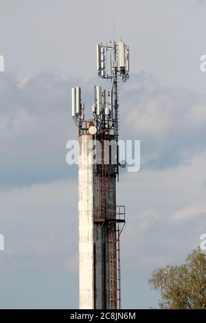 Vecchio camino industriale di calcestruzzo sporco con scalini di metallo arrugginito sopra un lato e recinzione di sicurezza sulla parte superiore riempito di densamente antenne per telefoni cellulari montate Foto Stock