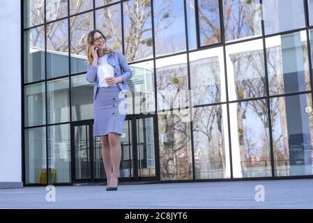Giovane uomo d'affari che parla al telefono mentre cammina di fronte di un edificio di uffici Foto Stock
