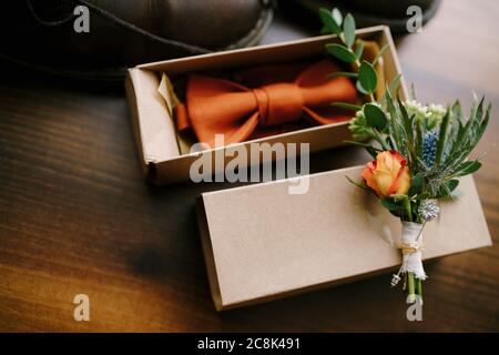 Cravatta con arco arancione in un pacchetto regalo con un bocciolo per lo sposo. Foto Stock