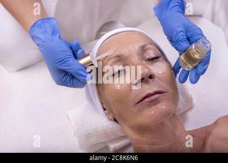 Closeup di bella donna anziana che applica siero di faccia in un salone di bellezza Foto Stock