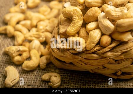 Noci di anacardi in un cesto di vimini e noci di anacardi sparse su tela di tela con una superficie di tessitura ruvida. Primo piano Foto Stock