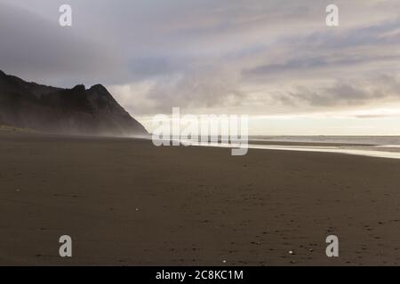 Vista delle montagne nella costa meridionale dell'Oregon, mentre cadono nel Pacifico con cieli grigi e un pizzico di luce proveniente da sotto la nebbia Foto Stock