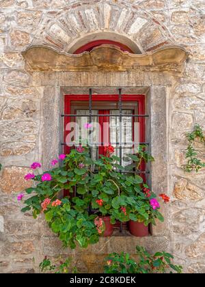 Effimero ed Eterno. Fiori di geranio colorati su una finestra secolare. Camminando nei vicoli medievali di Pyrgi, Isola di Chios, Grecia Foto Stock