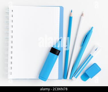 Notebook bianco vuoto e pennarelli blu con matite e penna su sfondo bianco. Disposizione piatta, mockup. Foto Stock
