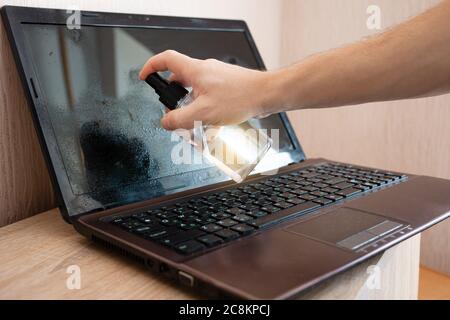 L'uomo pulisce il computer portatile da polvere e batteri con spray imbevuto di alcool. Disinfezione, protezione contro il coronavirus, pulizia in casa. La ragazza wip Foto Stock