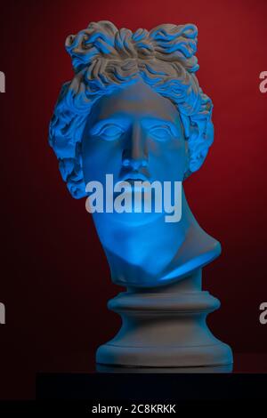 Statua di un busto della testa di Apollo in blu locale chiaro su uno sfondo rosso scuro Foto Stock