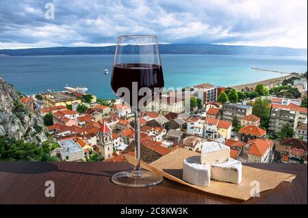 Bicchiere di vino rosso con formaggio brie vista sulla piccola città di Omis circondata da montagne, fiume Cetina e mare, Riviera di Makarska, Croazia. Foto Stock