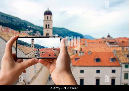 Turista che scatta foto del centro di Dubrovnik. Uomo che tiene il telefono e scattare foto dei tetti rossi dalle mura della città di Dubrovnik Foto Stock