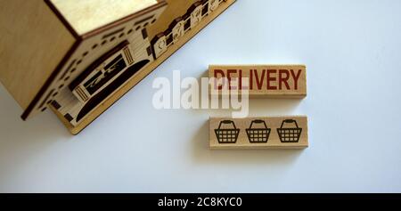 Blocco di legno forma la parola 'consegna' e l'icona cestino di cibo vicino casa in miniatura. Splendido sfondo bianco, spazio per la copia. Concetto di consegna a domicilio. Foto Stock