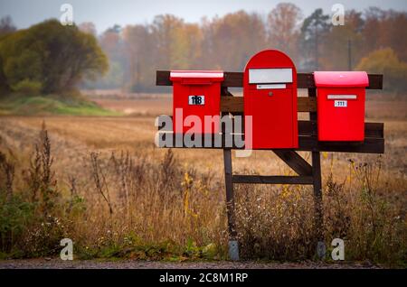 Tre caselle di posta rosse in campagna vicino a un campo autunnale Foto Stock