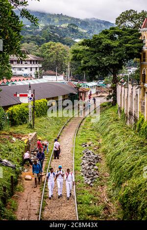 Gli studenti camminano lungo i binari del treno fuori dalla stazione ferroviaria di Kandy in Sri Lanka Foto Stock