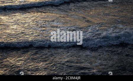Primo piano di onde dalla scogliera, la luce del sole tramontante cade in modo che sembra un placer d'oro sulla superficie del mare Foto Stock