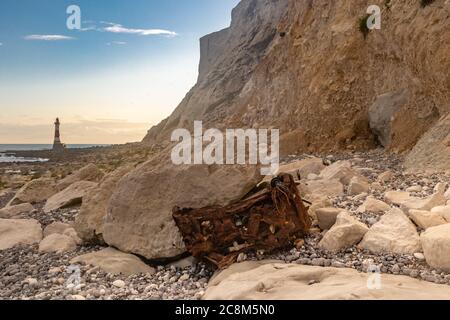 I resti arrugginiti di un'auto in fondo a scogliere di gesso in Sussex, con il faro di Beachy Head in lontananza Foto Stock