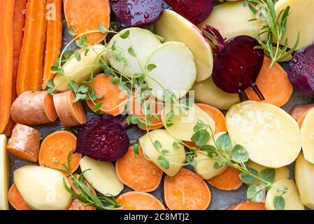 Tagliare le verdure crude prima di metterle in forno. Carote, patate, patate dolci, barbabietole, kohlrabi, rosmarino, aglio, issopo Foto Stock