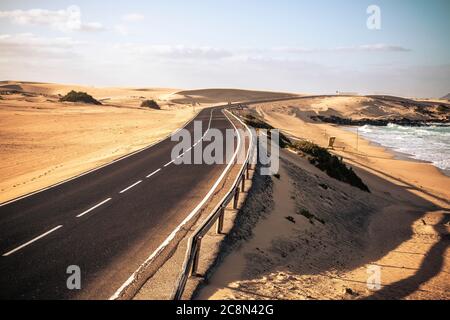 Lunga strada asfaltata nera con deserto e spiaggia intorno per viaggi e avventura stile di vita estivo concetto con nessuno che viaggia e no auto da traffico - bea Foto Stock