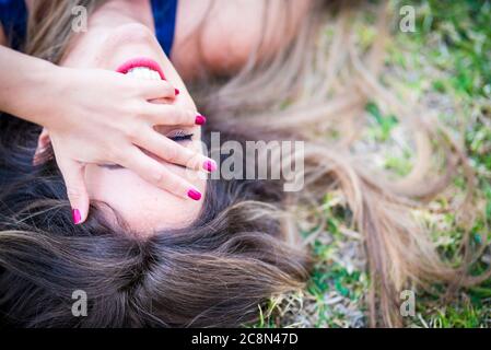 Primo piano ritratto da sopra di una bella ragazza caucasica allegra che ride molto e che ha un sacco di divertimento a disposizione sull'erba in tempo libero all'aperto ac Foto Stock