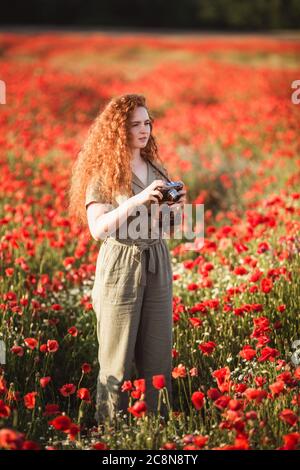 Giovane bella ragazza rossa-hear scatta le foto nel campo rosso dei fiori di papavero Foto Stock