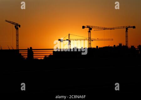 Le gru di costruzione sopra il paesaggio urbano contro un tramonto Foto Stock