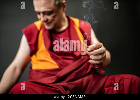Monaco buddista in rosso kesa, tenendo in mano un bastone di incenso con incenso Foto Stock