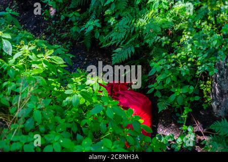 Un telone rosso piegato si trova in un fossato tra i campi gettati via nella bella natura Foto Stock