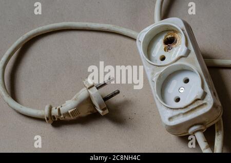 Condizione della spina elettrica, presa dopo scossa su fondo marrone. Presa multipla bianca dopo cortocircuito. Sicurezza elettrica. Foto Stock