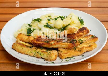 Semplici zucchine fritte impanate in casa o bastoncini di zucchine e insalata di patate in piatto bianco su tavolo da picnic in legno Foto Stock